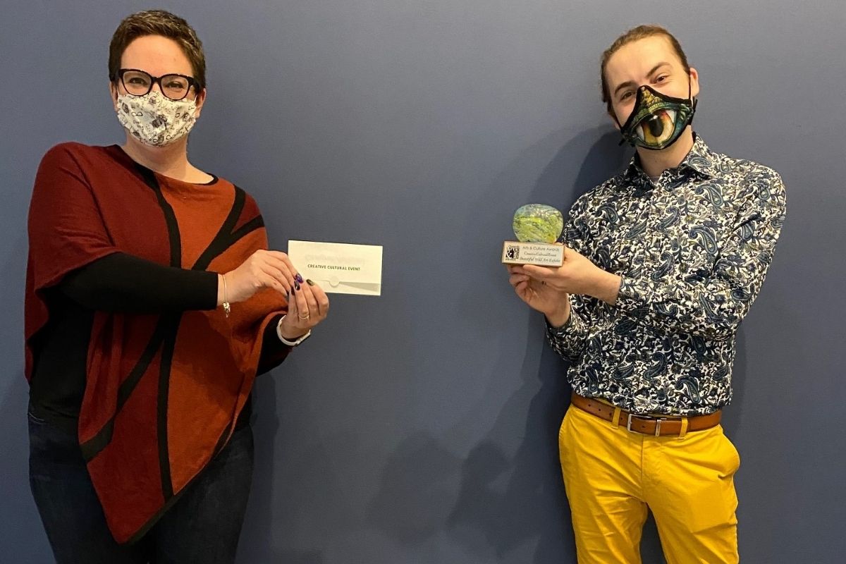 Woman presenting a man with an award. Both individuals are wearing masks.